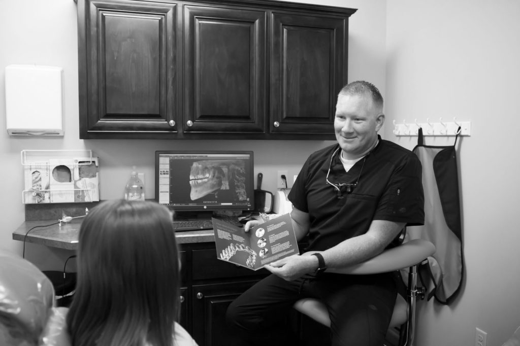 dentist holding a cosmetic dentistry booklet open while talking to a dental patient