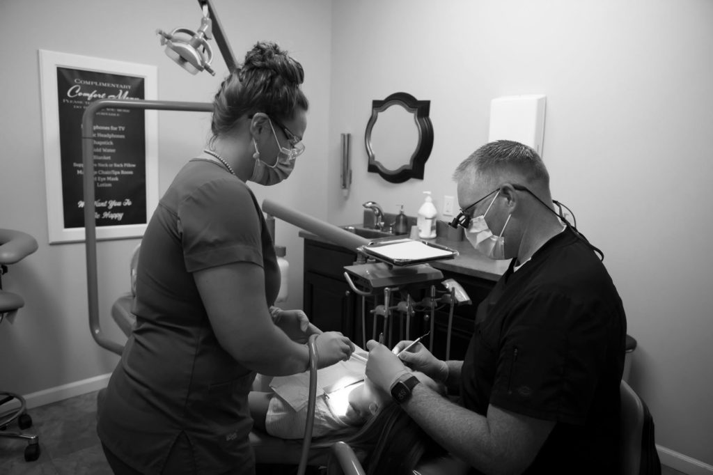 dentist examining a patient's teeth while a dental assistant helps
