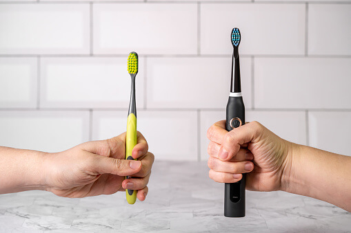 a hand holding a toothbrush next to a hand holding electric toothbrush
