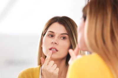 A woman looking at her reflection in a mirror and closely examining her teeth