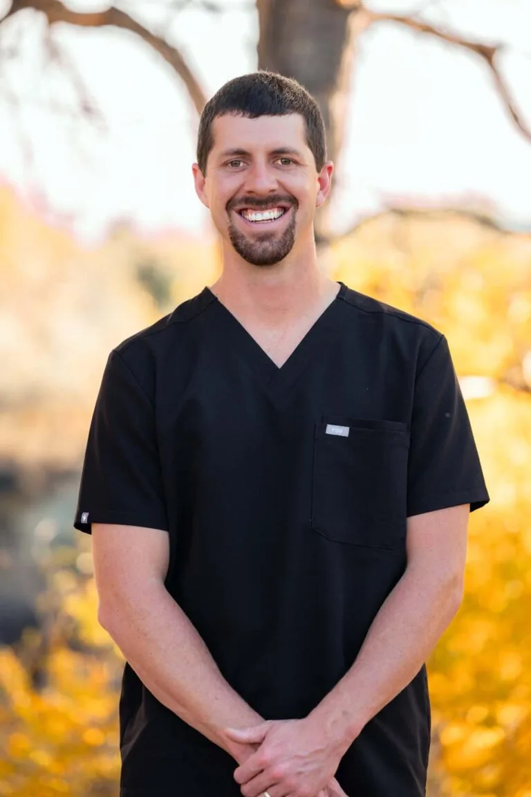 The image shows a photo of Dr. Shultz wearing a black scrubs with his hands on the front, the background is outdoor.